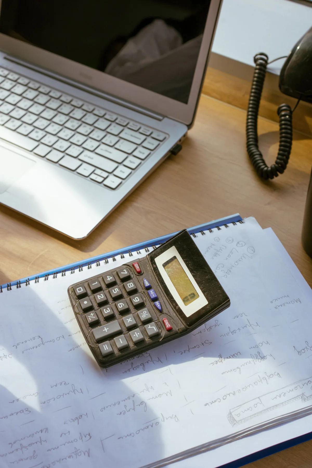 Calculator and notebook beside a laptop.