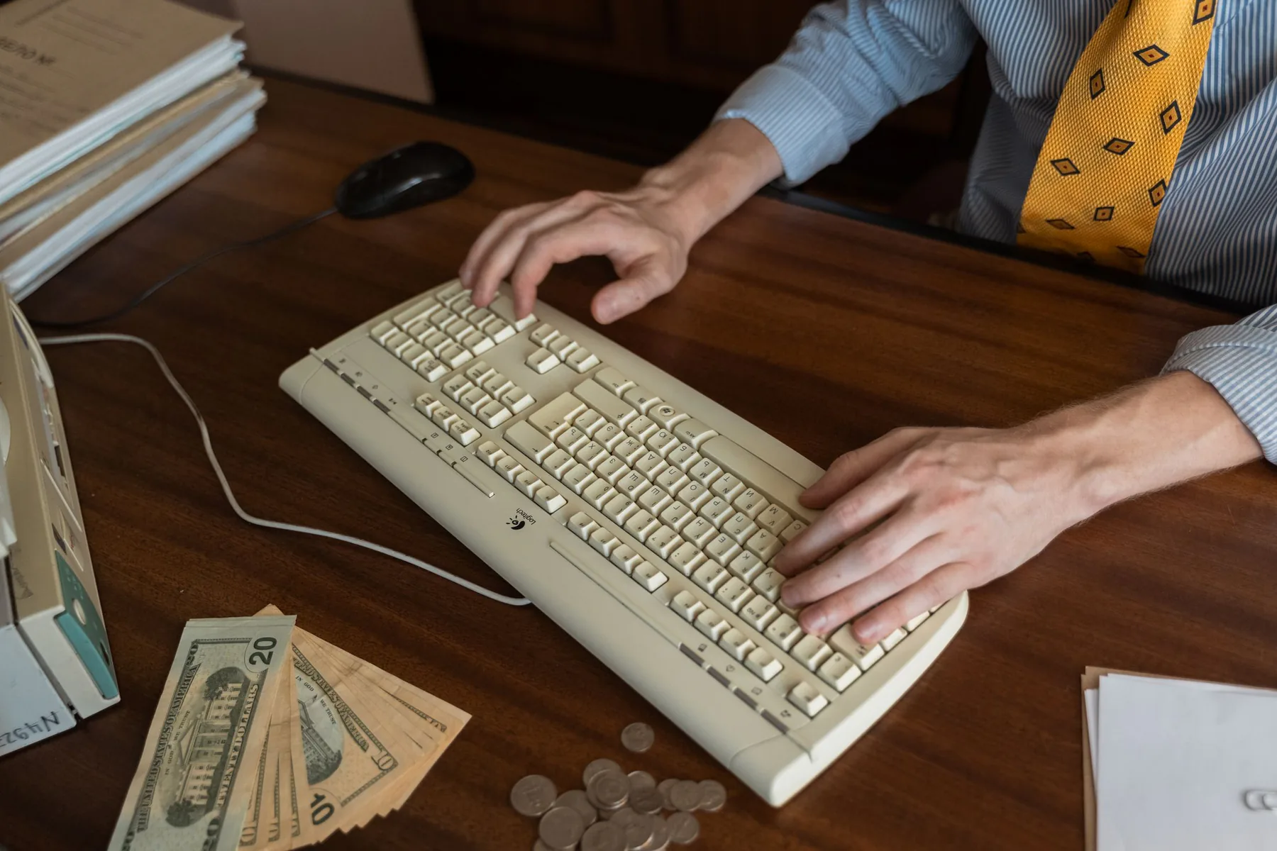 Hands at a computer keyboard beside cash and coins.
